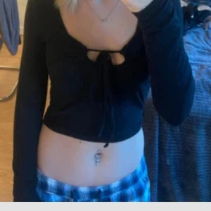 Svart långärmad topp Noisy May - Svart långärmad topp från Noisy May med snygg knytning framtill och djup urringning. Modellen är croppad och har en smickrande passform som framhäver midjan. Perfekt för dig som gillar trendiga och stilrena plagg.