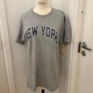 Grå New York t-shirt Fruit of the Loom - Snygg grå t-shirt från Fruit of the Loom med stort svartvitt 'NEW YORK'-tryck över bröstet. Köpt i USA. Ny men tvättad. Medium herr men funkar på tjejer med. Mjuk bomullsblandning. Perfekt för en avslappnad streetstyle-look. Hämtas i Hägersten eller skickas. 