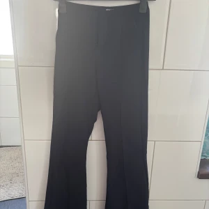 Mörk blå bootcut kostymbyxor Gina Tricot - Snygga svarta kostymbyxor från Gina Tricot med bootcut-snitt. Byxorna har hög midja och klassisk pressveck framtill. Perfekta för en clean och stilren look. Materialet känns mjukt och följsamt. Storlek XS. Köparen står för frakten. 