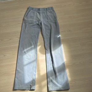 Juicybyxor - Snygga ljusblå mjukisbyxor med bred resår i midjan och stora framfickor. Byxorna har en rak passform och är gjorda i mjukt fleecematerial, perfekta för chill dagar. Diskret broderad logga på ena fickan. Liten defekt på en av benen med inget som syns mycket