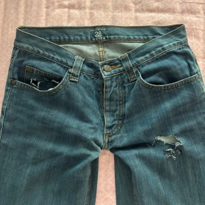 Lowwaist jeans med sliten design  - Säljer ett par blå jeans med hål på framsida och fickor, väldigt trendigt. 
