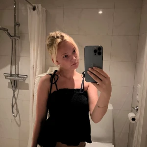 Marinblå linnetopp med knytband - Supersöt marinblå linnetopp med smockad överdel och knytbara axelband. Toppen har en lätt volang nertill och är perfekt för varma dagar. Sitter bekvämt och ger en avslappnad men ändå trendig look.