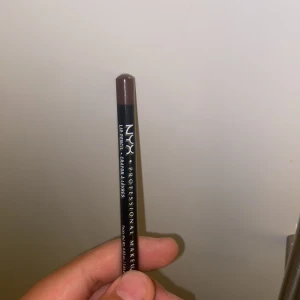 NYX brun läppenna - Helt ny. Säljer en brun läppenna från NYX Professional Makeup. Pennan har en klassisk träkropp och ger en snygg, definierad läppkontur med sin djupa bruna nyans. Perfekt för att skapa fylligare läppar eller kombinera med ditt favoritläppstift.