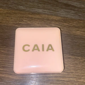 CAIA persikofärgad rouge - Rouge från CAIA i en snygg persikoton. Kommer i en stilren, ljusrosa fyrkantig dosa med spegel i locket. Perfekt för att ge kinderna en fräsch och naturlig glow. Pressat puderformat som är lätt att applicera.