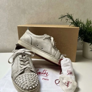 Christian Louboutin vita sneakers med nitar (storlek 45) - Säljer ett par Christian Louboutin sneakers, ganska använda, har limmat fast lite på sidan, går fortfarande att fräscha till. Snören, dustbag, extra nitar och box ingår. Kom med bud! 