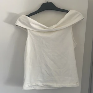 Vit offshoulder topp från UNIQ STUDIO -  vit offshoulder topp från UNIQ studio. Toppen har en bred, vikt krage som ger en snygg draperad effekt över axlarna. Tillverkad i mjukt bomullstyg. Den är ganska tajt i storlek 170 så skulle säga att den sitter som en xs/xxs. Aldrig använd.