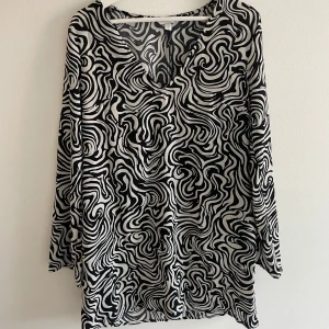 Mönstrad Svartvit klänning - Säljer en flowy svartvit klänning med v-ringning och långa ärmar. Blusen har ett coolt grafiskt mönster och är tillverkad i ett lätt, mjukt tyg som faller snyggt. Perfekt för dig som gillar att sticka ut med grafiska prints.Svart och vit mönstrad klänning med vida ärmar.  Går lite ovanför knäna för mig som är 168cm. från H&M i storlek M. Mycket bra skick, använd 1 gång. Jag har massor av artiklar till salu, köp 