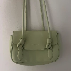 Ljusgrön axelväska  - Snygg ljusgrön axelväska med stilrena knyt-detaljer framtill. 