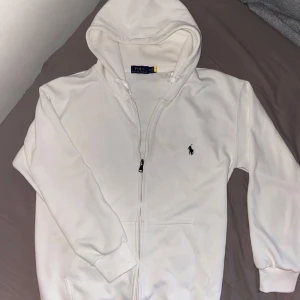 Vit hoodie från Polo Ralph Lauren - Snygg vit hoodie från Polo Ralph Lauren med dragkedja och klassisk logga på bröstet. Tröjan har huva med snörning, långa ärmar och två fickor framtill. Storlek S-M köpt själv på Plick