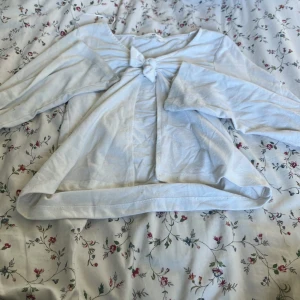 Vit långärmad topp med knyt från H&M - Supersöt vit långärmad topp från H&M med knyt framtill. Toppen har en lätt croppad passform och är gjord i mjuk bomull. Perfekt för dig som gillar en enkel men ändå trendig look med fina detaljer.