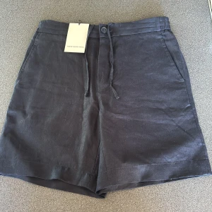 Mörkblå linneshorts These Glory Days - Snygga mörkblå linneshorts från These Glory Days i modell Volt. Shortsen har snörning i midjan, sidfickor och bakfickor med knapp. Perfekta för varma dagar med sin luftiga känsla och stilrena look.