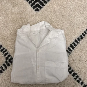 Vit linneskjorta från Zara - Snygg vit skjorta från Zara i luftig linne, perfekt för varma dagar. Klassisk krage, bröstficka och knäppning framtill. Enkel och stilren design som passar till många olika outfits.