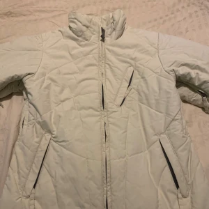 Vit pufferjacka från Fiberstone S - Snygg vit pufferjacka från Fiberstone i storlek S. Jackan har hög krage, flera dragkedjeförsedda fickor och quiltad design. Materialet är syntet och jackan är vattentät, perfekt för kalla dagar. Insidan är fodrad i mörkblått tyg för extra komfort.