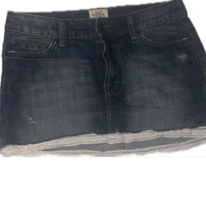 Jeanskjol med spets volang  - Snygg kort jeanskjol från h&m i mörkblå denim med klassiska fickor och bälteshällor. Kjolen har en vit spetskant längst ner som ger en extra cool touch. 