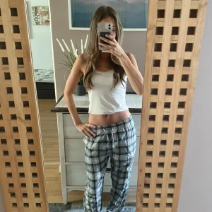 Grå-rutiga pyjamasbyxor  - Säljer ett par grå och vita rutiga mjukisbyxor med snörning i midjan. Byxorna har avslappnad passform och är perfekta för chill dagar hemma. Mjukt material och elastisk midja för extra komfort.