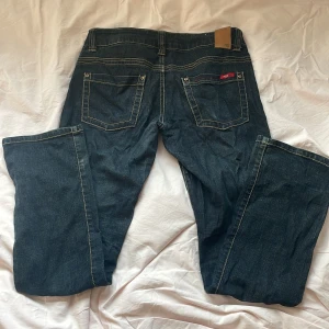 Blå bootcut jeans från Only - Snygga mörkblå jeans från Only med bootcut passform och kontrastsömmar. Klassisk femficksmodell med låg midja och detaljerade bakfickor. Jeansen är gjorda i mjukt denimtyg och har en metallknapp framtill. Bra skick, normal storlek 🤗36/32, passar som S/M. Jag är 163 cm lång. 
