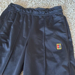 Svarta nikebyxor - Svarta träningsbyxor med elastisk midja och broderad färgglad logga på låret. Byxorna har smal passform och dragkedjor vid bensluten för enkel av- och påtagning. Perfekta för sport eller chill dagar.