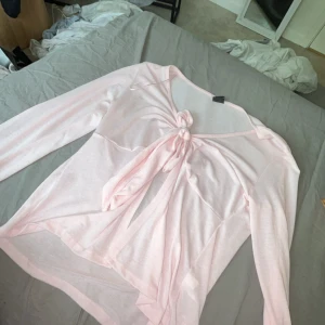 Ljusrosa långärmad topp Gina Tricot - Supersöt ljusrosa långärmad topp från Gina Tricot med knyt framtill. Tunn och luftig, perfekt för lager på lager eller som statement-piece. Snyggt croppad passform och mjukt material som känns skönt mot huden.