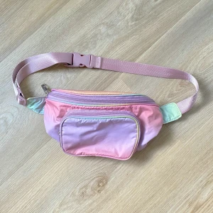 Pastellfärgad magväska med dragkedjor - Säljer en snygg magväska i pastellfärger med rosa, lila och mintgröna toner. Väskan har två fack med dragkedja och justerbart band med spänne. Perfekt för att bära mobilen och småprylar när du är på språng.