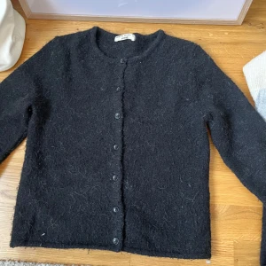 Svart kofta i ull från Gina Tricot XS - Mysig svart kofta från Gina Tricot i borstad ullmix. Klassisk rak modell med rund halsringning och knappar hela vägen framtill. Perfekt att slänga över en t-shirt eller ha som lager när det är kyligt ute.