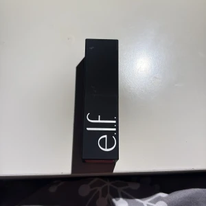 e.l.f. O Face Satin Lipstick Pleased - Snyggt satinläppstift från e.l.f. i nyansen Pleased. Kommer i en stilren, svart fyrkantig hylsa med vit logga. Färgen är en djup, bärig röd som ger en mjuk och krämig finish på läpparna. Perfekt för dig som vill ha ett pigmenterat och återfuktande läppstift.