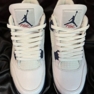 Nike Air Jordan 4 Midnight Navy - Nike Air Jordan 4 sneakers i vitt skinn med grå och marinblå detaljer. Snygg mesh på sidorna, specklad grå häl och klassisk Jumpman-logga. Tjock sula med synlig Air-enhet och coola plastdetaljer vid snörningen. Perfekta för dig som gillar streetstyle.