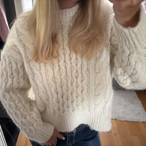Vit stickad kabeltröja med grov struktur - Säljer en chunky vit stickad tröja med grovt kabelmönster och ribbad kant vid hals, ärmslut och nederkant. Perfekt för hösten! 