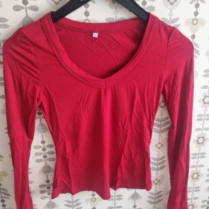 Röd långärmad tröja med v-ringning - Snygg röd långärmad tröja i mjuk bomull med v-ringad hals. Perfekt för dig som gillar enkel och stilren design. Passar dig som vill ha en smickrande och bekväm passform. Tröjan är tunn och lätt, vilket gör den enkel att matcha med dina favoritjeans eller kjol.