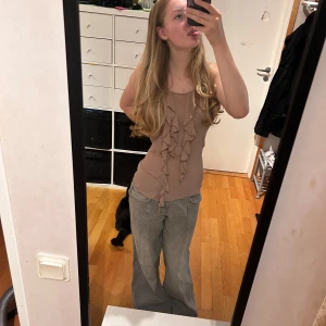 Beige linnetopp med volangdetaljer - Säljer en beige linnetopp med volanger framtill. Toppen är ärmlös  Materialet känns lätt och luftigt, perfekt för varmare dagar. Volangdetaljerna ger en extra touch och gör toppen unik. Passar bra säkerhetsnål där bak om man vill att den ska sitta tajt som bilden då den är lite lös. Använder inte. Storlek M o sparsamt använd.