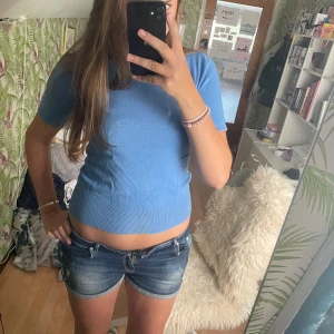 Blå kortärmad tröja från Zara - Snygg ljusblå tröja från Zara i storlek M. Modellen är kortärmad med rund hals och har tre dekorativa guldiga knappar i nacken. Materialet är mjukt och stickat, perfekt för dig som gillar enkel och clean stil. Passar dig som vill ha en basic topp med lite extra detaljer. Den har lite nopprig med inget som syns så mycket. Säljer då den inte kommer till användning.🤗💕