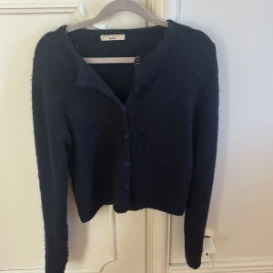 Mörkblå kofta från Gina Tricot - Säljer en mörkblå, fluffig kofta från Gina Tricot i storlek S. Koftan har rund hals, långa ärmar och knäppning med svarta knappar framtill. Materialet är mjukt och stickat, perfekt för kyliga dagar. Enkel och stilren design som är lätt att matcha.