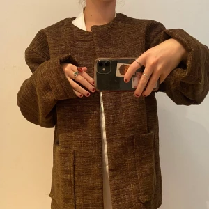 Brun oversized jacka - Säljer en brun oversized cardigan jacka med grov textur och stora fickor framtill. Jackan har en rak passform och långa ärmar, perfekt för lager-på-lager-stil. Enkel och stilren utan synliga knappar eller dragkedja.