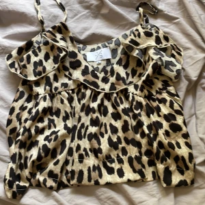 Leopardmönstrad linnetopp från JS Millenium - Säljer en snygg linnetopp från JS Millenium i leopardmönster. Toppen har tunna axelband och volangdetaljer längs urringningen. Färgerna går i beige och svart, och materialet känns lätt och svalt – perfekt för varma dagar.