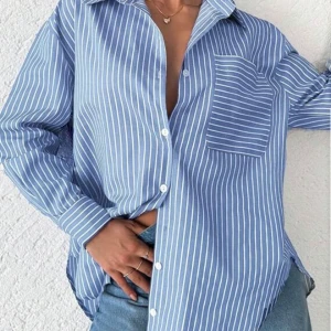 Blåvit randig skjorta med ficka - Snygg blå skjorta med vita vertikala ränder och en bröstficka med horisontella ränder. Klassisk krage, långa ärmar och knappar framtill. Perfekt att bära till jeans för en chill och fräsch look. Materialet känns lätt och skönt mot huden.