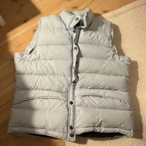 Ljusblå dunväst Peak Performance M - PRIS KAN SÄNKAS/DISKUTERAS! Ljusblå dunväst från Peak Performance i storlek M. Västen har  broderad logga på bröstet och stängs med tryckknappar. Två fickor framtill. Trendig och perfekt för hösten, vintern och våren  och  lager-på-lager under kyliga dagar. 