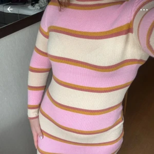 Randig stickad klänning från The Frolic strl38, rosa beige  - Superfin stickad kortklänning från The Frolic i storlek 38. Klänningen har breda ränder i rosa, beige och senapsgult, med långärmad och rund hals. Den är figurnära och mjuk, perfekt för dig som gillar färg och retrovibbar.