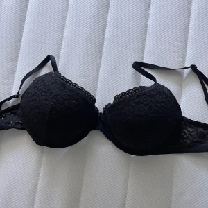 Svart spetsig push-up BH från H&M - Svart BH från H&M med snygg spetsdetalj över hela kuporna och längs kanterna. Axelbanden är smala och justerbara. Den har mycket vadd för push-up och är bekväm. Säljer även likadan Bh i svart. Vid frågor hör av dig!