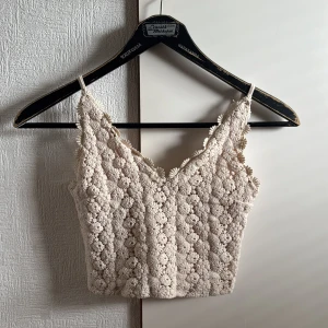 Beige virkad linnetopp från Topshop - Supersöt beige linnetopp från Topshop med virkade blommor och smala axelband. Toppen har en croppad passform och v-ringning framtill. Perfekt för sommarens alla tillfällen och ger en boho-vibe till din outfit.