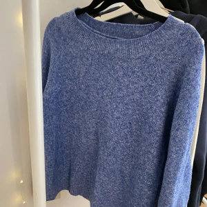 Blå stickad tröja med rund hals - Mysig blå stickad tröja med rundad hals och ribbade muddar. Perfekt för kyliga dagar och enkel att matcha med jeans eller kjol. Tröjan har en klassisk, loose passform och långa ärmar som ger en avslappnad vibe.