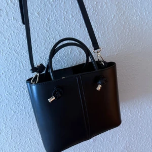 Zara väska - Snygg svart axelväska med både axelrem och handtag. Väskan har stilrena metalldetaljer i guld. Invändigt finns dragkedja för extra säkerhet. Perfekt storlek för det viktigaste och passar till många outfits. Från Zara, inga defekter.
