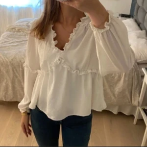 Vit volangblus från vero moda  - Supersöt vit blus från Aware/ vero moda med volangdetaljer längs v-ringningen och luftiga ärmar. Hittar inte längre på deras hemsida därav lånade bilder💕 endast använd 1 gång så är i nysckick, säljer för 200kr💗