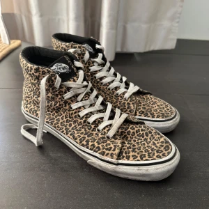 Vans leopardmönstrade höga sneakers - Snygga höga sneakers från Vans med leopardmönster i beige och svart. Skorna har vita snören, svart innerfoder och klassisk vit sula med svart rand. Så snygga att piffa upp med i en basic outfit!