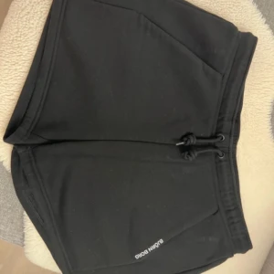 Svarta shorts från Björn Borg - Svarta shorts från Björn Borg med snörning i midjan och två stora fickor framtill. Perfekta för träning eller chill, med en enkel och stilren design. Mjukt material som känns skönt mot huden och diskret logga på ena benet.