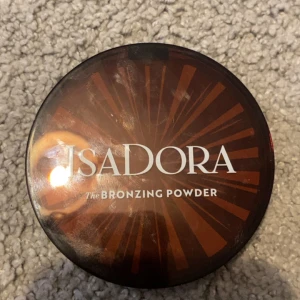 Isadora Bronzing Powder  - Snygg bronzer från Isadora i nyansen Beach Tan, perfekt för att ge ansiktet en solkysst glow. Kommer i en rund brun plastförpackning med spegel och pressat puder med Isadora-logga. Vegansk, doftfri och kliniskt testad. Innehåller 10 g, använd några fåtal gånger. 