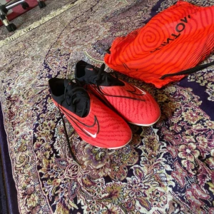 Nike Phantom Gx röda fotbollsskor - Säljer ett par Nike Phantom Gx fotbollsskor i rött och svart med coola grafiska detaljer. Skorna har snörning, spetsig tå och platt sula med dobbar för grymt grepp på planen. Ovandelen är i syntetmaterial och innersulan är röd med Phantom-tryck. Perfekt för dig som vill sticka ut på matchen!          Skicka om ni har frågor😊