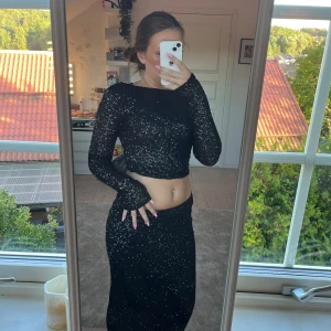 Svart glittrig långklänning med slits - Säljer ett svart sätt med tröja och kjol med glittriga paljetter över hela tyget. Perfekt för dig som vill sticka ut med en glam look.