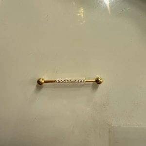 Crystals Industrial Barbell guld - Snygg industrial barbell från Wildcat i guldigt stål med glittrande kristaller längs mitten. Stavens längd är 34 mm och kulorna är 5 mm. Perfekt för dig som vill ha lite extra bling i din piercing.