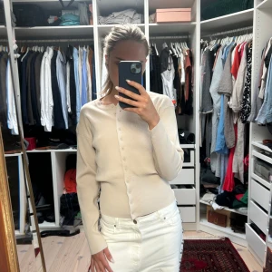 Beige ribbad kofta med knappar - Snygg beige kofta med ribbad midja och långa ärmar. Den har rund hals och knappar hela vägen framtill, vilket ger en clean och stilren look. Perfekt att matcha med jeans eller kjol för en chill och trendig vibe.