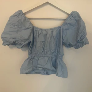 Ljusblå blus med puffärmar - Superfin ljusblå blus med bred resår vid axlarna och stora puffärmar. Modellen är croppad med volang nedtill och har en luftig känsla, perfekt för varma dagar. Passar dig som gillar romantisk och trendig stil.från bikbok. Strl xs. Går att pruta 