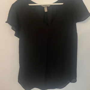 Svart blus med v-ringning H&M - En svart blus från H&M med v-ringning och korta, luftiga ärmar. Tunt och lätt material som ger ett snyggt fall. Perfekt att styla med jeans eller kjol för en clean look.strl 40 men känns som en m. Använd en gång. Går att pruta 